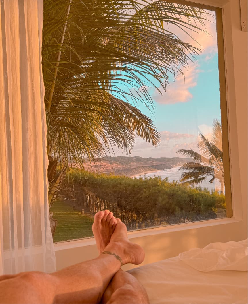 Hóspede relaxando na cama da villa com vista para palmeiras e a costa de Sibaúma