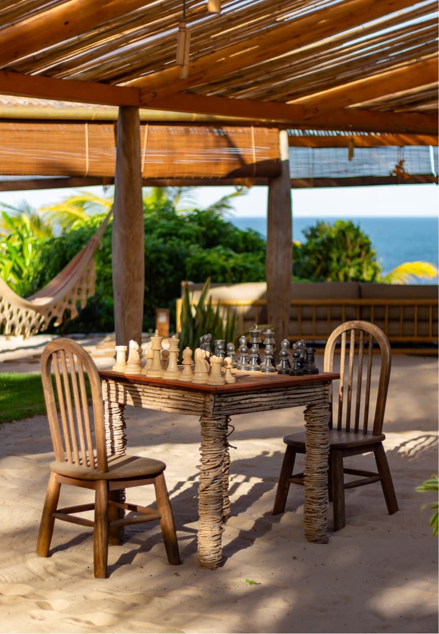 Mesa de xadrez rústica sob pergolado de madeira com vista para o oceano no Kilombo Villas