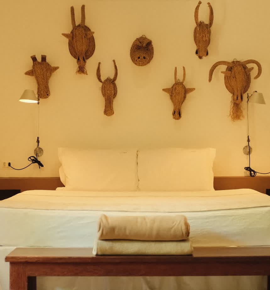 Kilombo Villas - villa Jacú Jardim - Quarto de hotel decorado com cabeças de animais de palha na parede, incluindo rinoceronte, gnu, anta, touro e cabeça de capivara, criando uma atmosfera rústica e temática de vida selvagem.