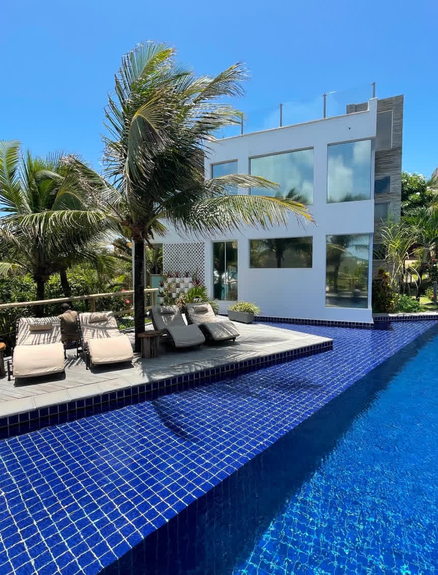 Vista aérea da arquitetura da villa Zumbi Master, mostrando a integração entre os andares, janelas panorâmicas que refletem a piscina azul e um solário privativo no topo com uma pequena piscina de hidromassagem quadrada.