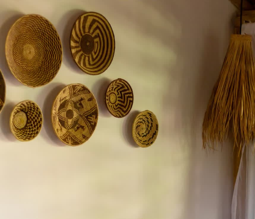 Kilombo Villas - villa Jacú Jardim - Conjunto de tapetes decorativos artesanais feitos de palha com diferentes padrões geométricos, decorando uma parede branca.