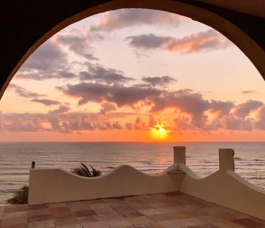 Kilombo Villas - Das Rosas - Vista de um pôr do sol na praia vista de uma varanda com arquibancada, nuvens coloridas no céu e mar calmo, transmitindo relaxamento e beleza natural.