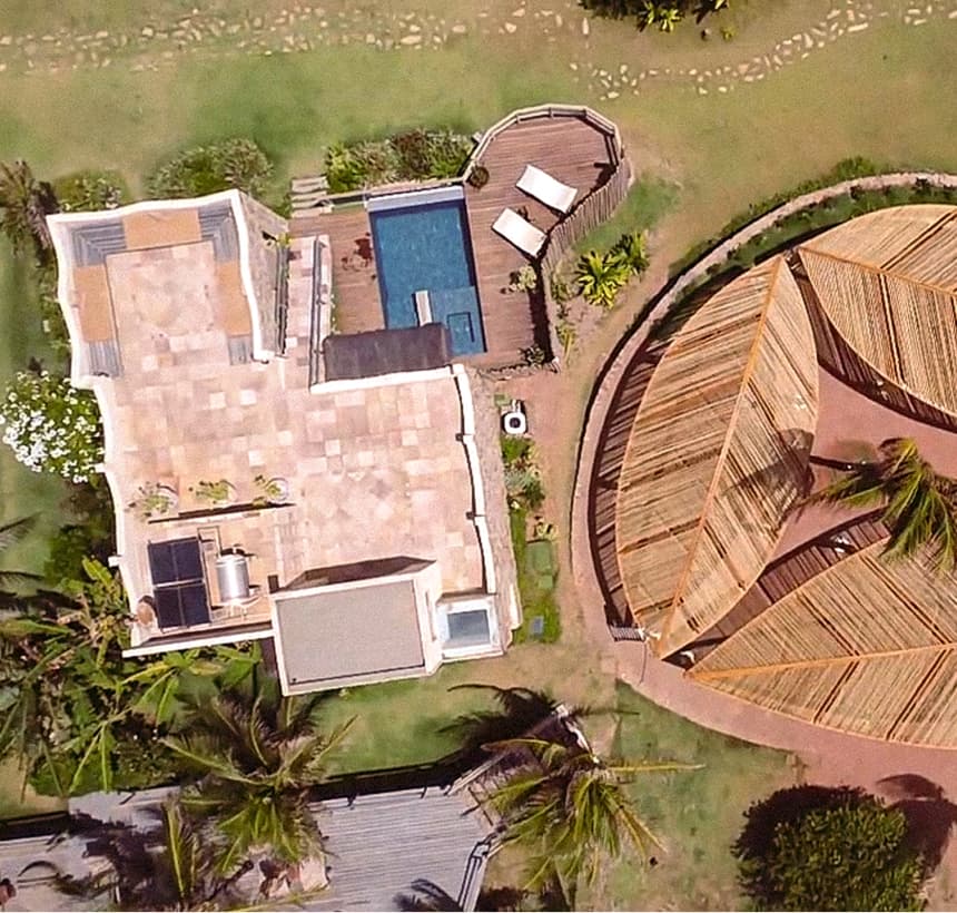 Kilombo Villas - Das Rosas - Interior aconchegante de uma casa de praia com móveis de fibras naturais, janelas amplas e vista para o mar ao fundo.