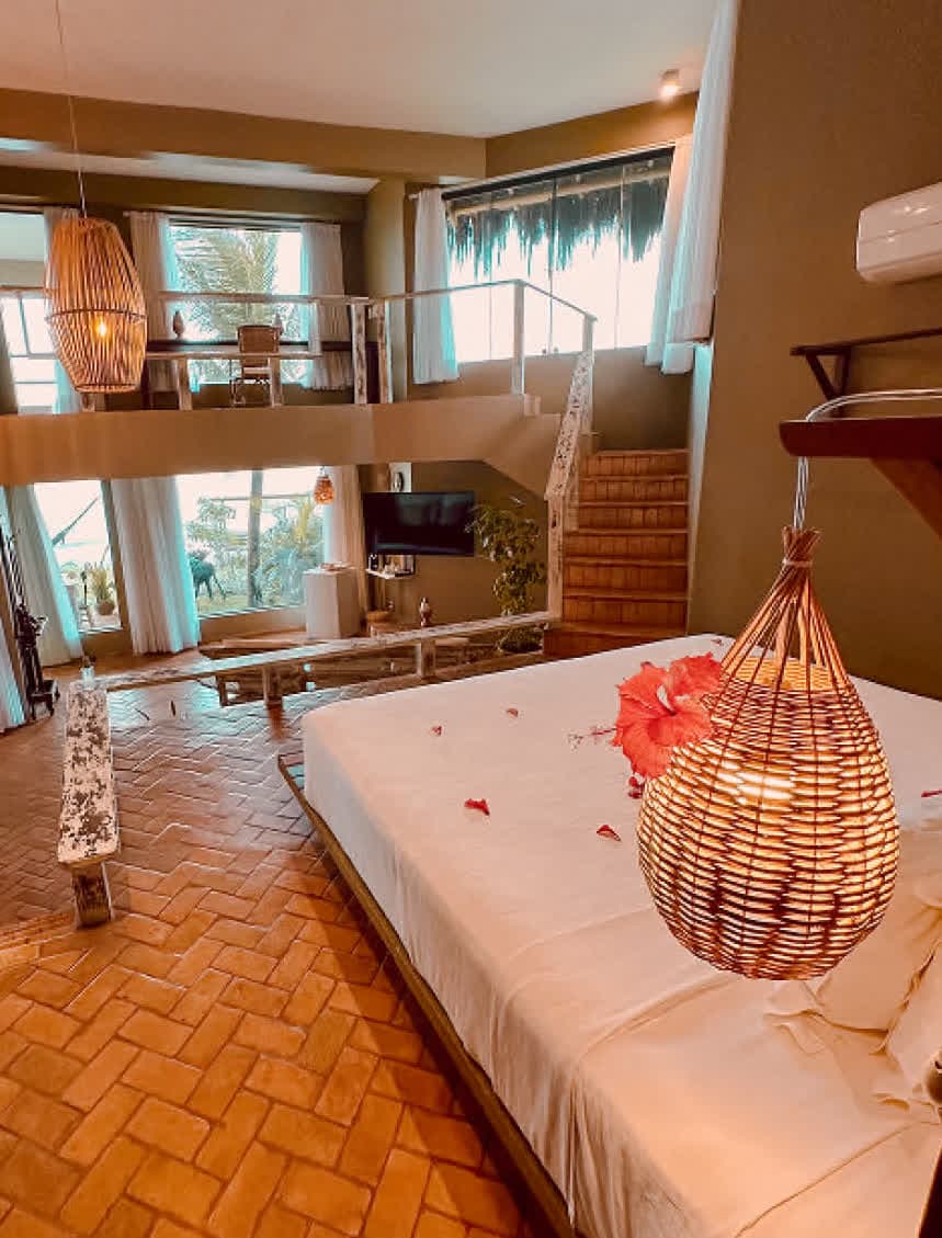 Kilombo Villas - villa Desidéria - Foto de uma academia em um apartamento com vista para o mar, contendo equipamento de musculação, bola de pilates, tapete de yoga e cenário de praia ensolarada ao fundo.