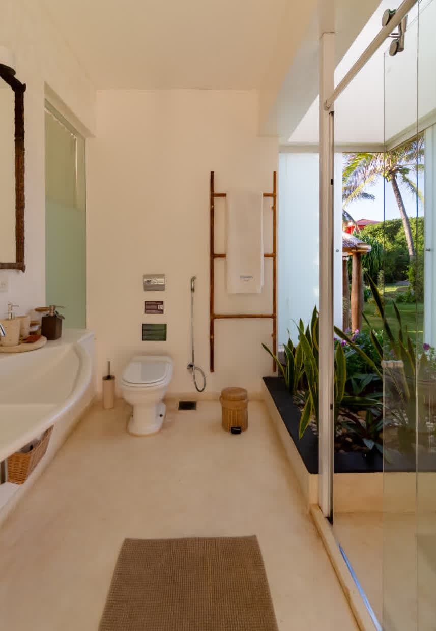 Kilombo Villas - Das Rosas - Banheiro com vista para o jardim tropical, shines de luz natural, decoração minimalista e detalhes em madeira para um ambiente acolhedor e arejado.
