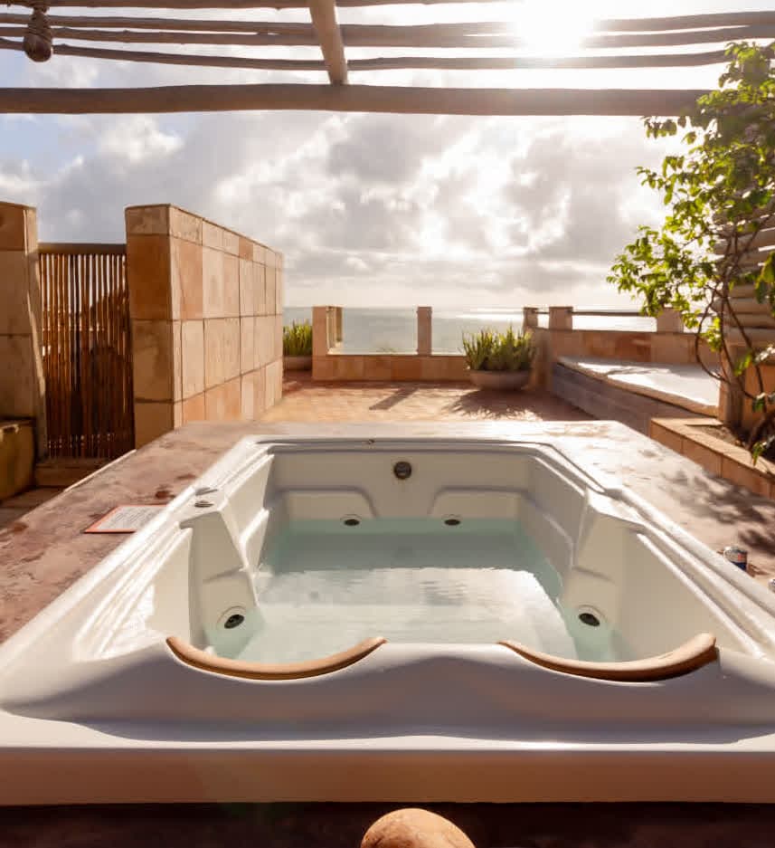Kilombo Villas - villa Desidéria - Banheira de hidromassagem ao ar livre em uma varanda com vista para o mar, decorada com plantas e revestimentos de pedra, em um dia ensolarado com céu parcialmente nublado.