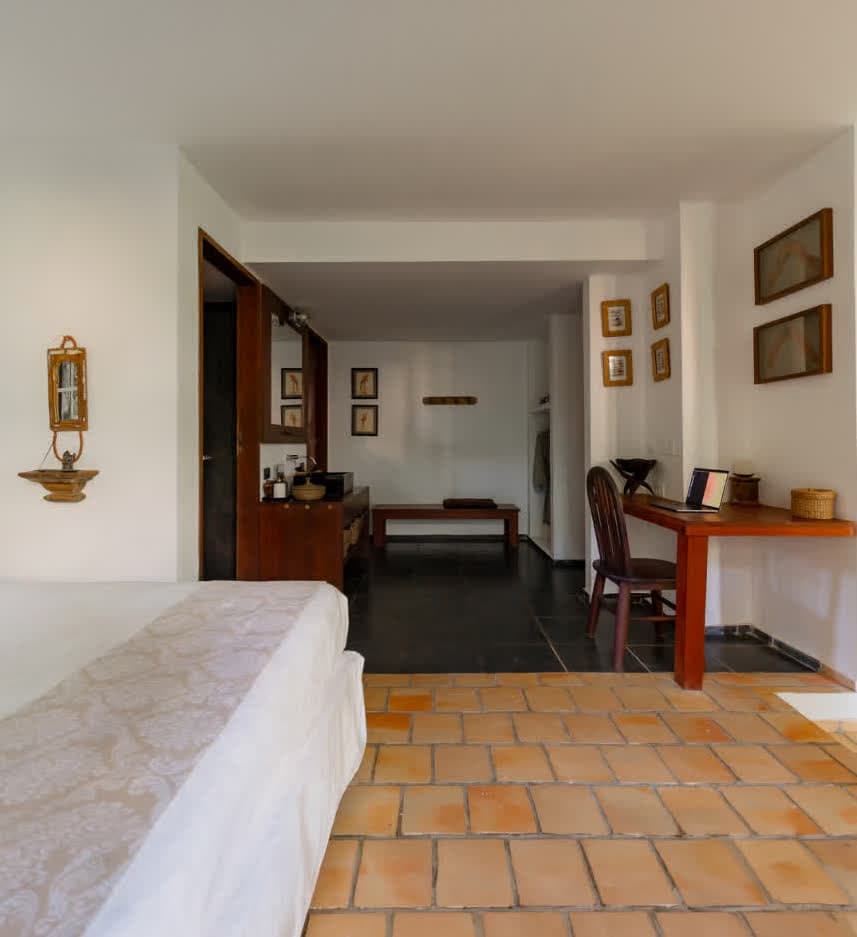 Kilombo Villas - villa Jacú Jardim - Imagem de uma mulher idosa usando um laptop sentado em uma cadeira e uma mulher mais jovem preparando café na cozinha, em um ambiente doméstico aconchegante.