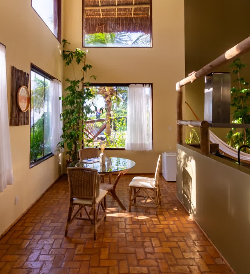 Kilombo Villas - villa Sibraáma Jardim - Varanda com móveis de fibra natural e piscina ao fundo, integrando o espaço ao ambiente tropical. O deck de madeira leva à área de lazer externa com vista para o jardim.