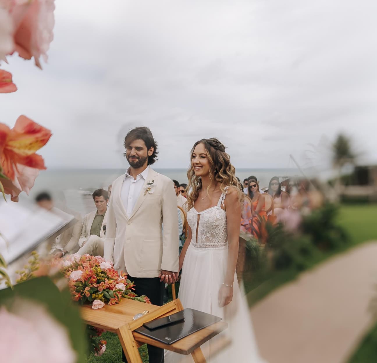 Noivos sorrindo durante a cerimônia com arranjo de flores coloridas e vista para o mar ao fundo no Kilombo Villas