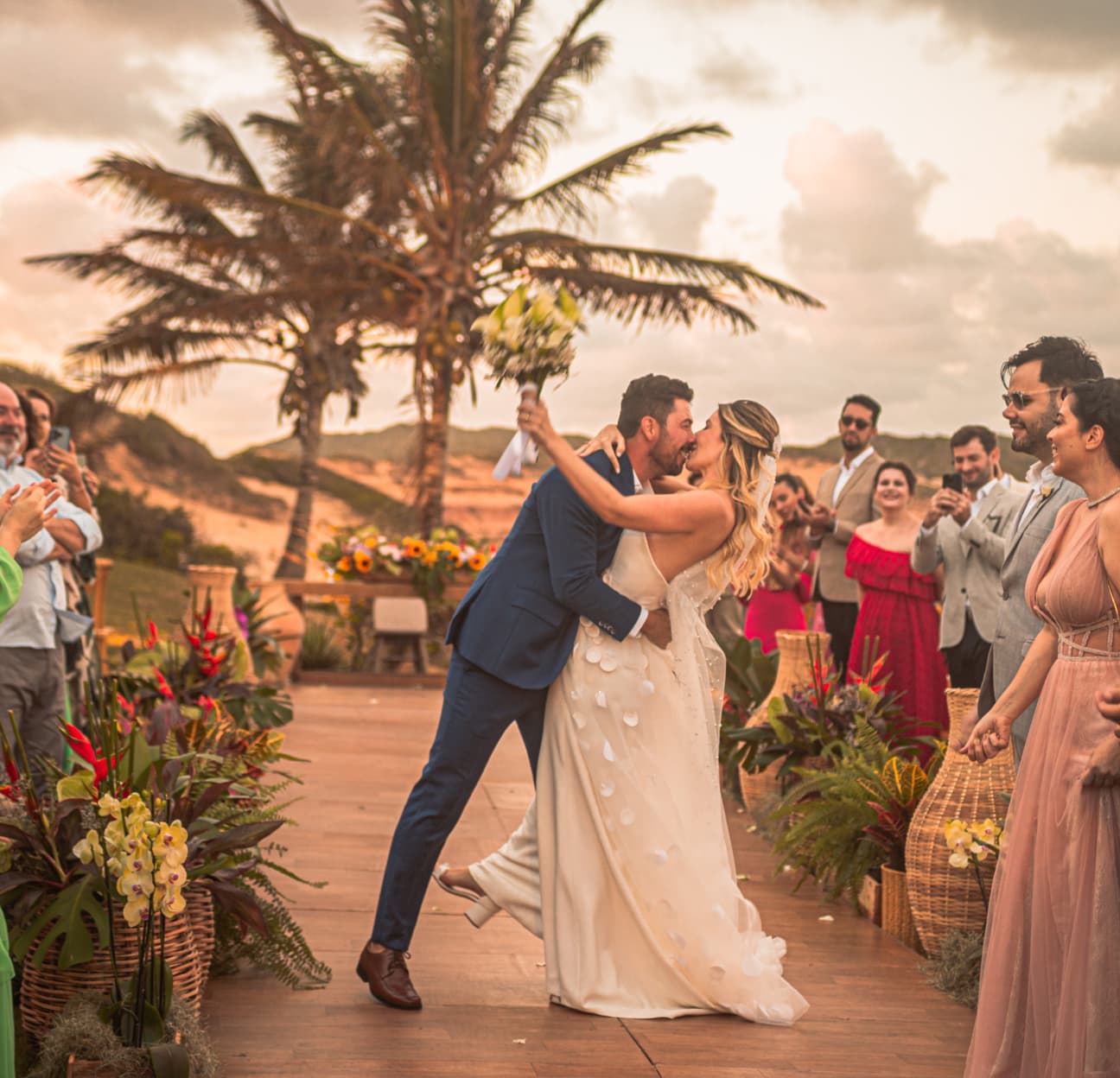 Noivos se beijando ao fim da cerimônia ao pôr do sol no Kilombo Villas, com convidados ao redor aplaudindo
