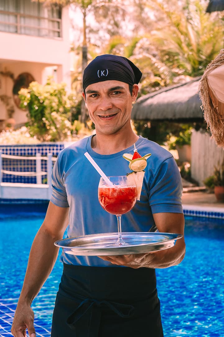 Mordomo do Kilombo Villas segurando uma bandeja com drink ao lado da piscina.