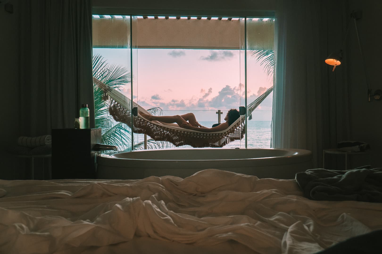 Hóspede descansando em rede na varanda de uma villa do Kilombo Villas com banheira e vista para o oceano ao entardecer