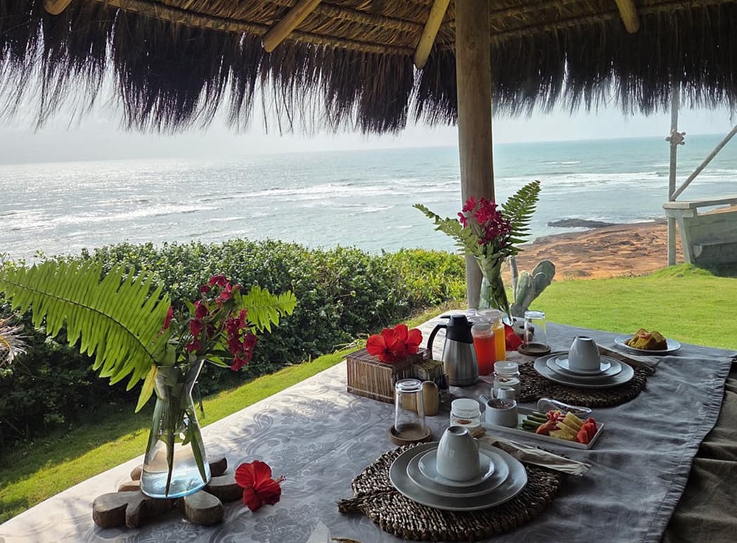 Mesa de café da manhã montada em pavilhão de palha com vista para o mar de Sibaúma