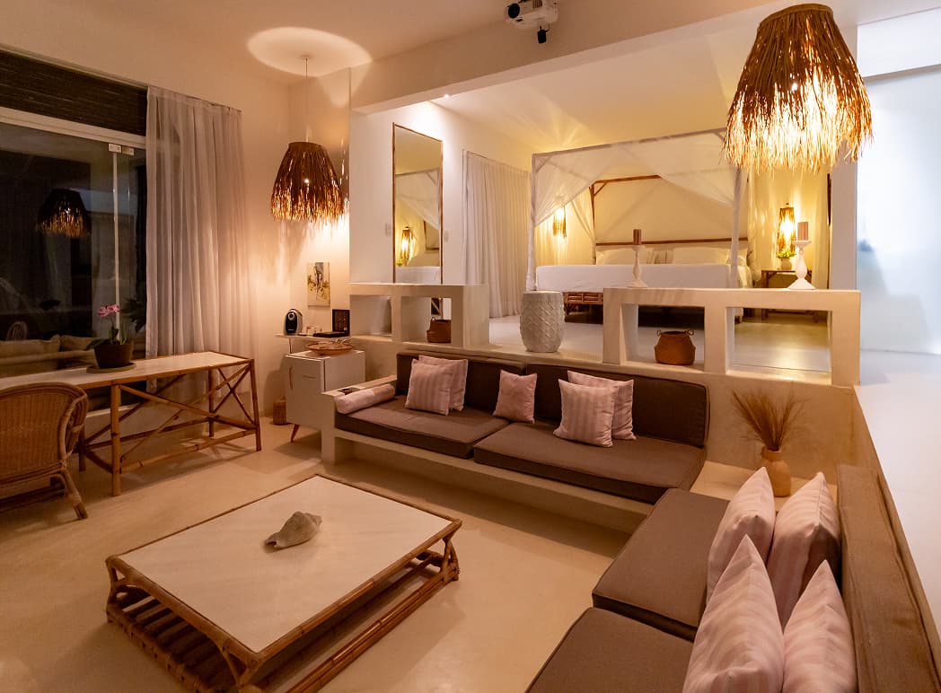 Sala de estar de villa com sofá em alvenaria, almofadas e luminárias de fibra natural no Kilombo Villas