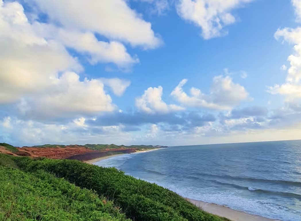 Vista aérea das falésias e da praia de Sibaúma sob céu azul, próximo ao Kilombo Villas