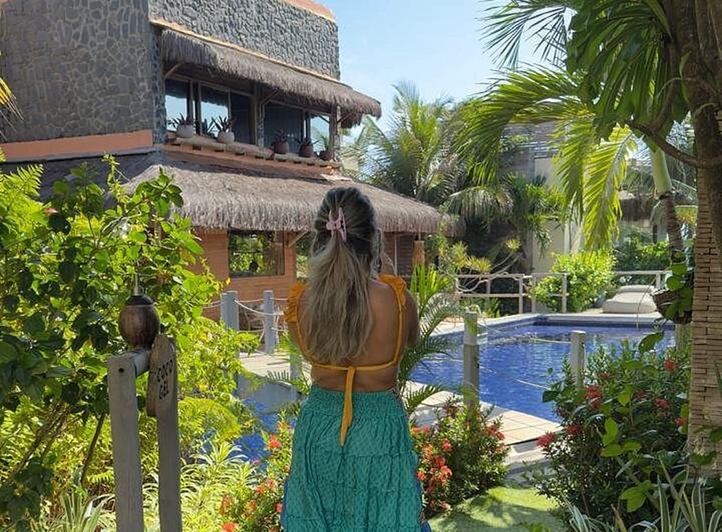 Hóspede em pé de costas observando villa com piscina e jardim tropical no Kilombo Villas