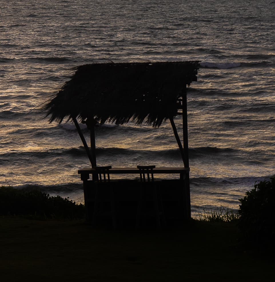 Quiosque de palha em silhueta à beira-mar durante o amanhecer no Kilombo Villas