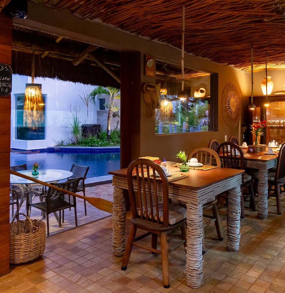 Salão do restaurante com mesas de madeira e vista para a piscina no Kilombo Villas