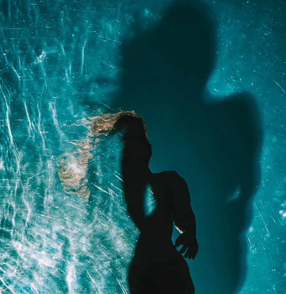 Silhueta de mulher refletida na água azul-turquesa da piscina do Kilombo Villas