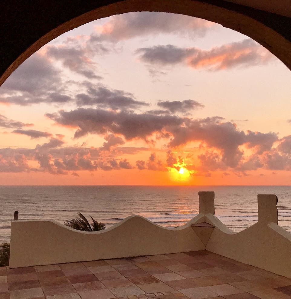 Pôr do sol sobre o mar visto do arco de uma villa do Kilombo Villas, em Pipa