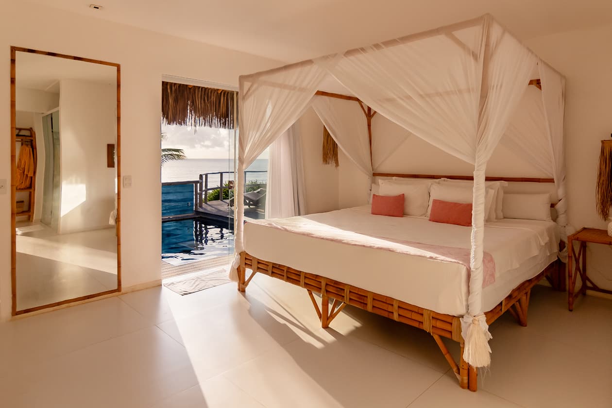 Suíte com cama de dossel em bambu e acesso direto à piscina privativa em villa do Kilombo Villas