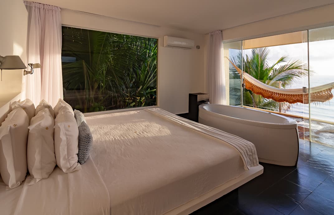 Quarto de villa com cama king, banheira de imersão e rede na varanda com vista para a mata e o mar no Kilombo Villas