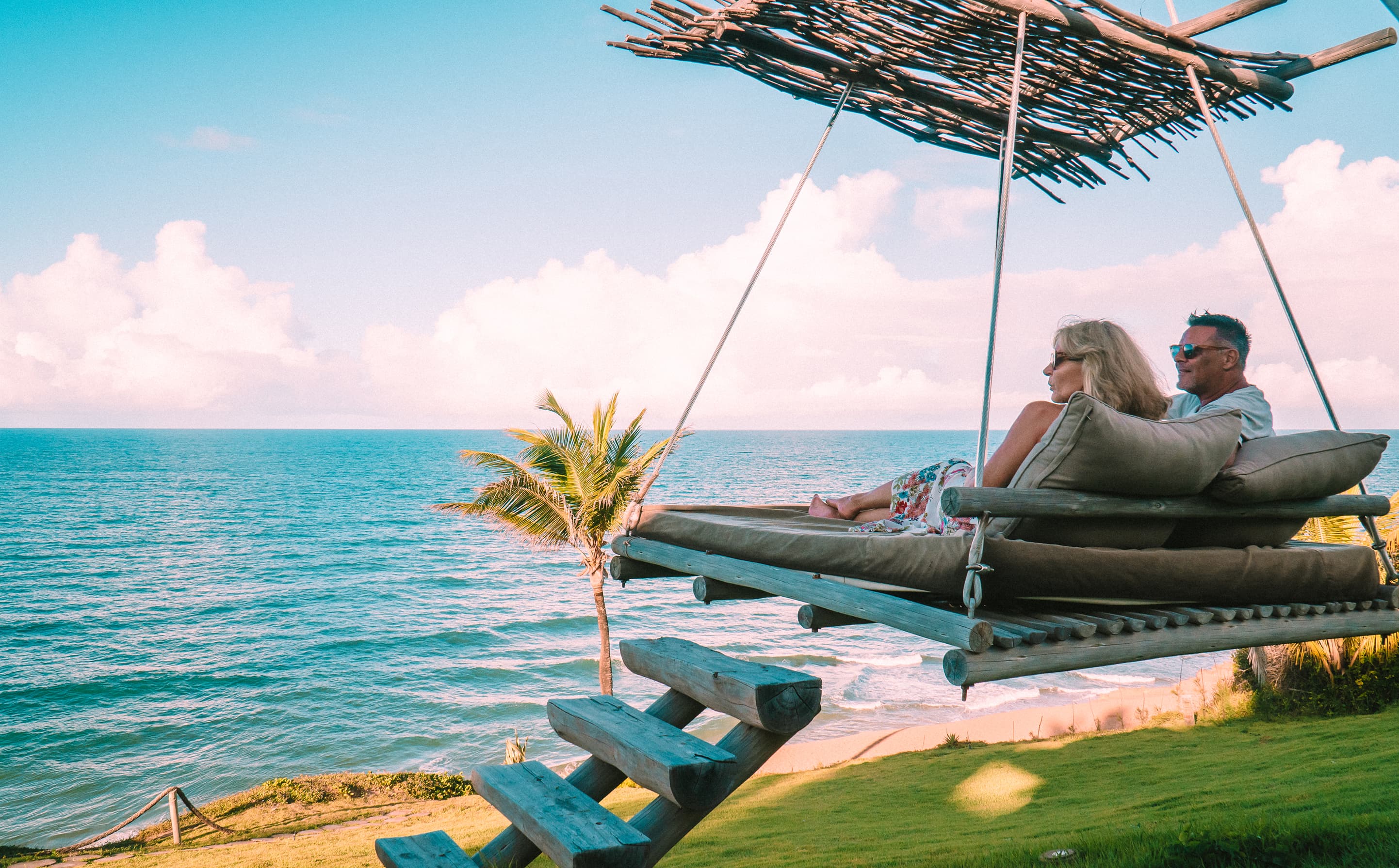 Casal relaxando em cama suspensa de madeira com vista para o oceano de Sibaúma no Kilombo Villas