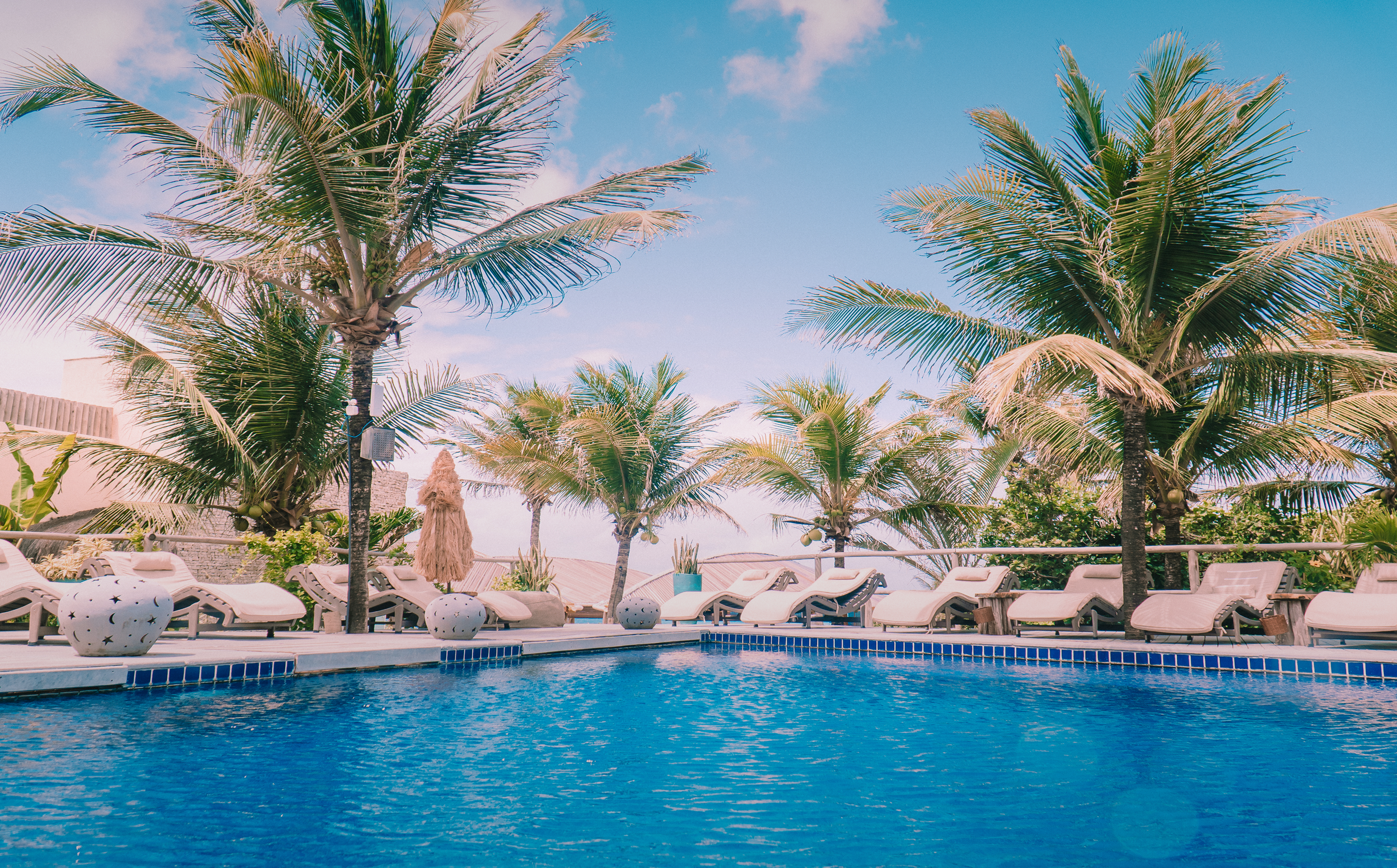 Piscina do Kilombo Villas com espreguiçadeiras, guarda-sol e palmeiras tropicais à beira-mar em Sibaúma