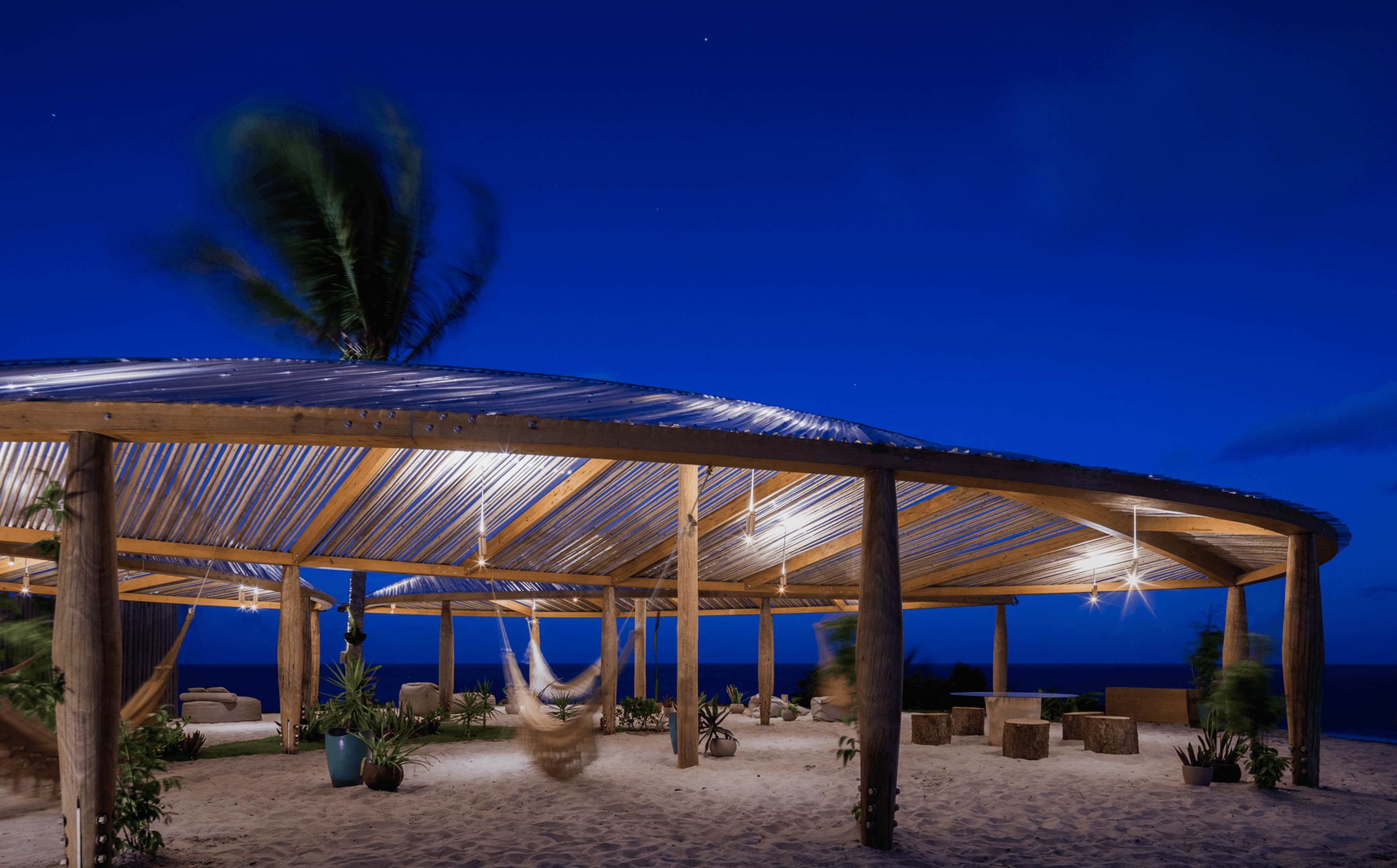 Pavilhão de madeira e bambu iluminado à noite com redes e vista para o oceano no Kilombo Villas, Sibaúma