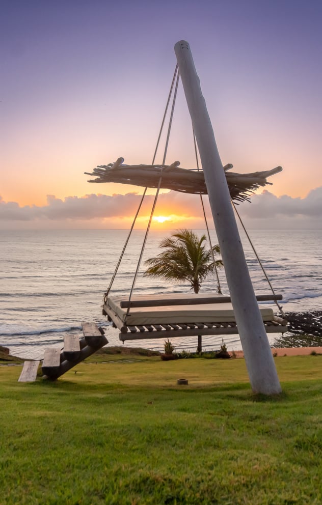 Wooden swing suspended at sunset with view for the sea and palm trees at Kilombo Villas, Sibaúma