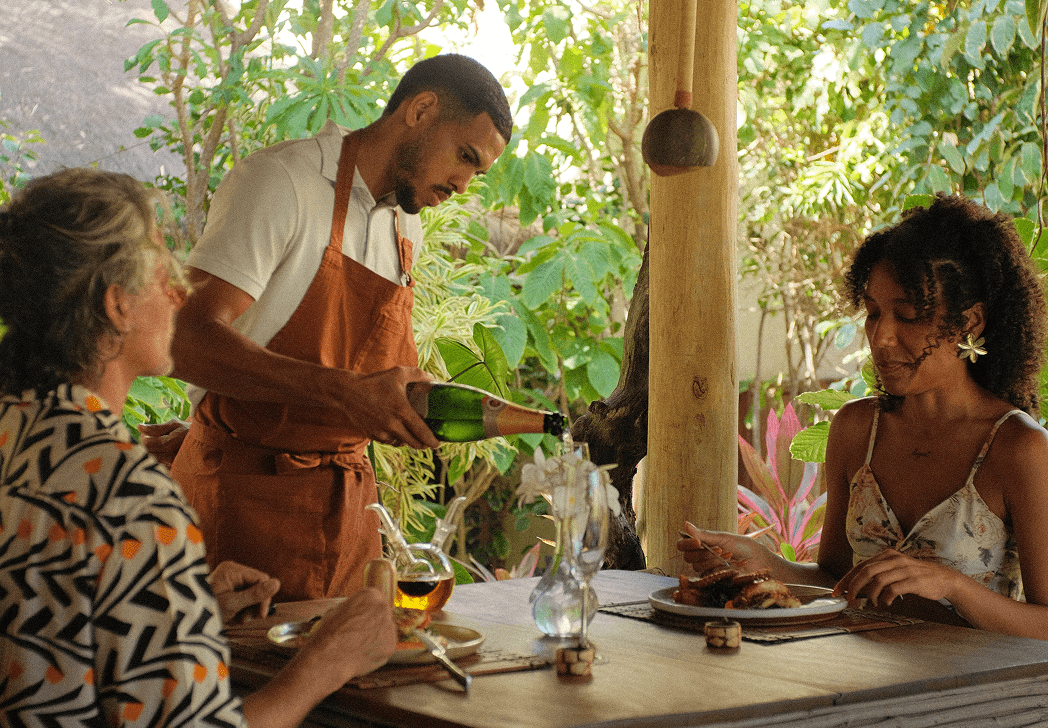 Garçom servindo vinho a hóspedes em mesa do Kibo Restaurante com ingredientes locais frescos, Kilombo Villas