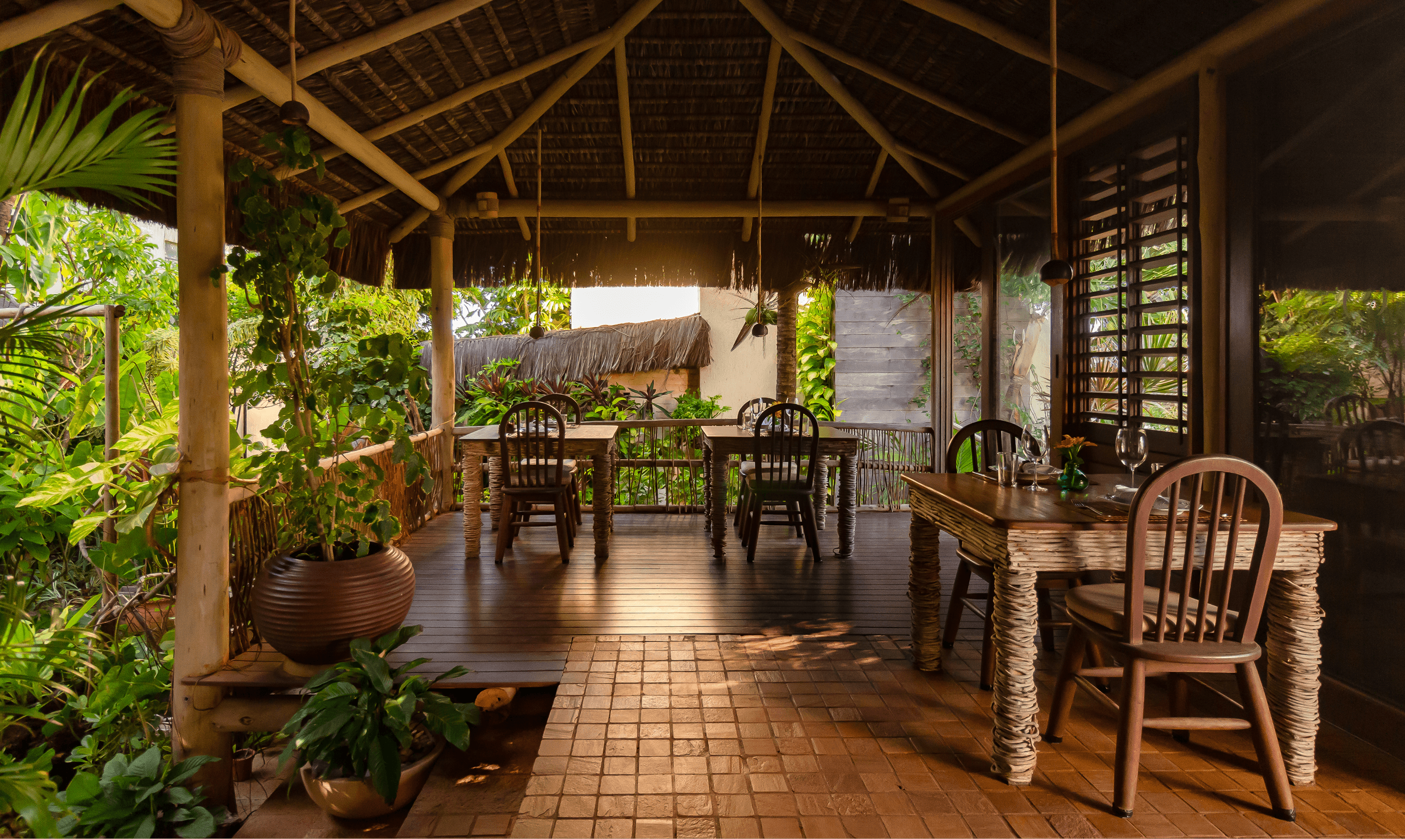 Salão aberto do Kibo Restaurante com mesas de madeira, plantas tropicais e teto de palha no Kilombo Villas