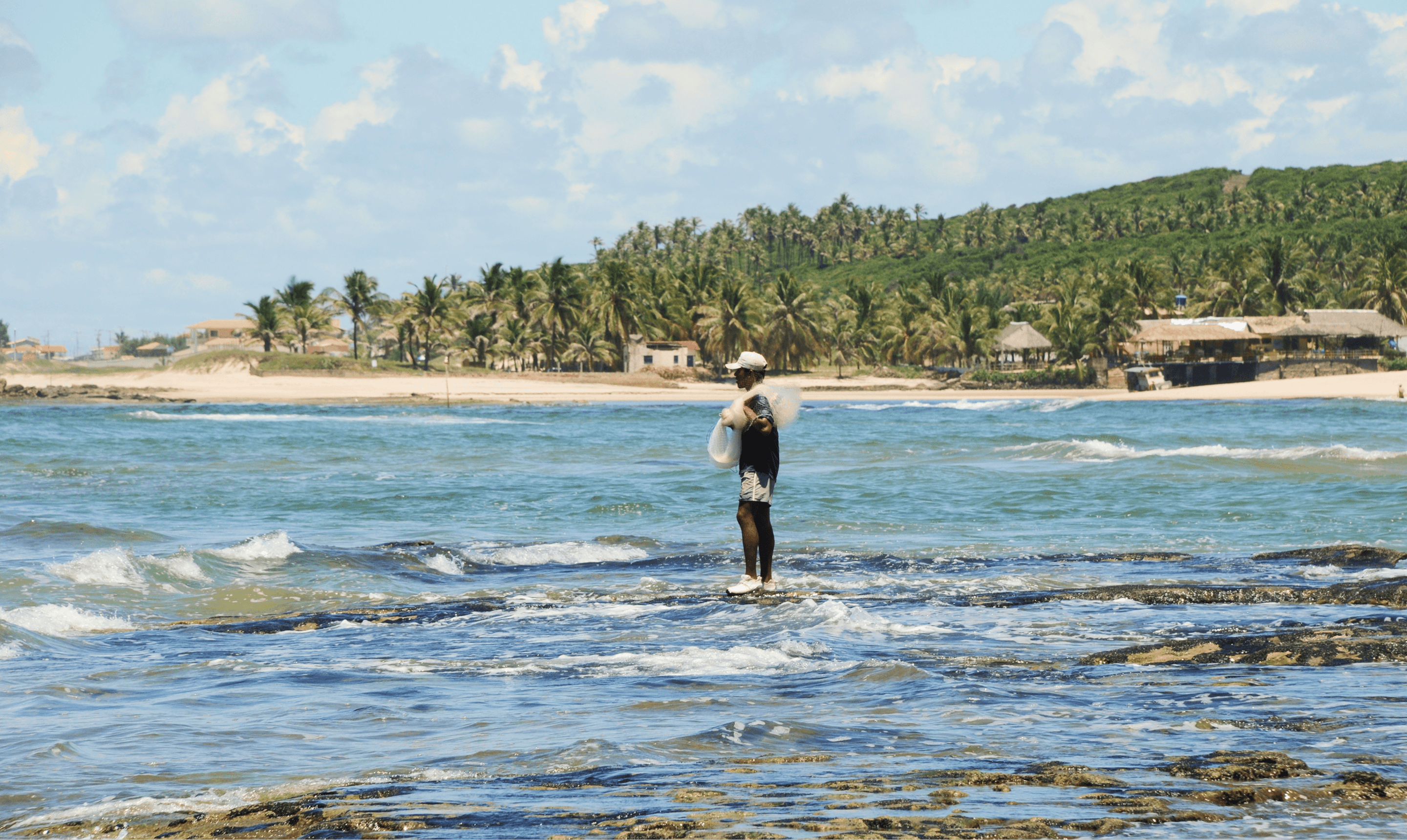 Pescador em pé no litoral de Sibaúma pescando com uma rede no ombro.
