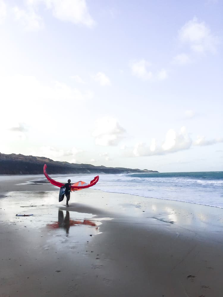 Kitesurfista carregando pipa colorida na areia da praia de Sibaúma com falésias e oceano ao fundo, próximo ao Kilombo Villas