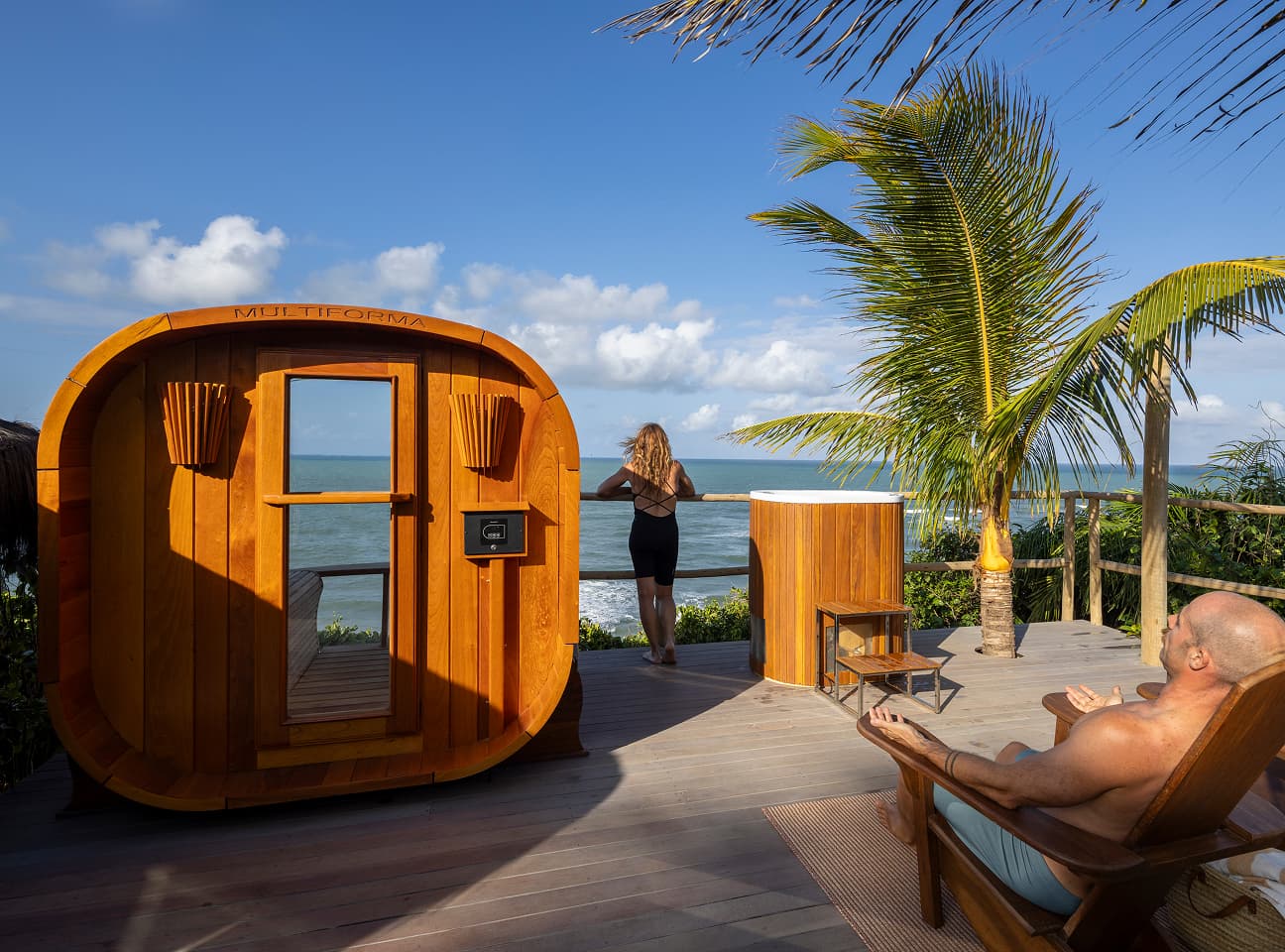 Sauna de madeira em deck com vista para o mar de Sibaúma, com hóspedes descansando ao lado de uma banheira de imersão