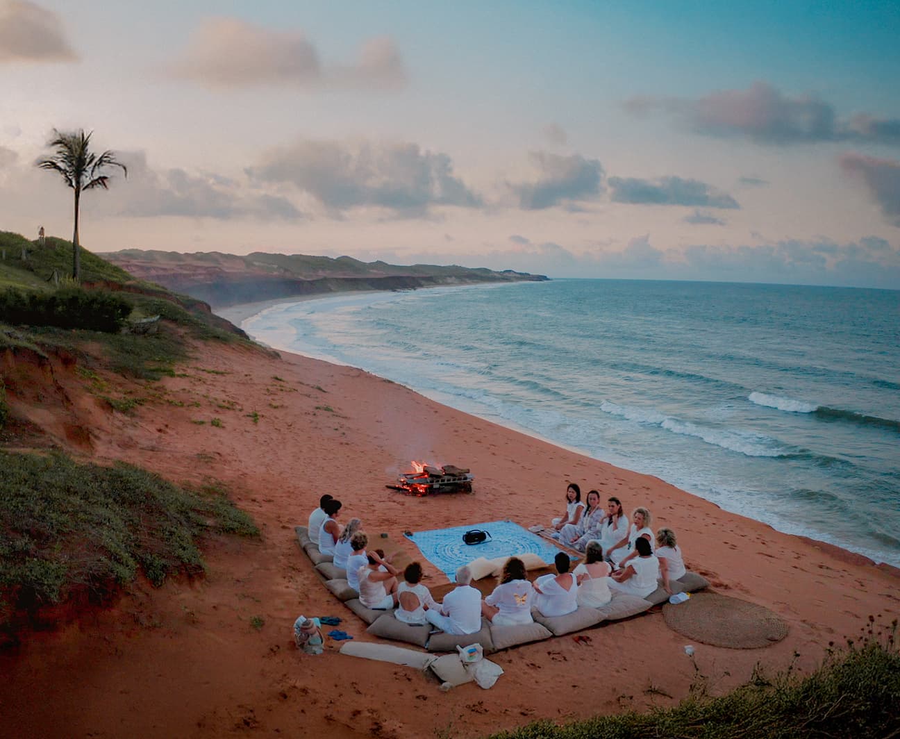 Grupo sentado ao redor de fogueira na praia de Sibaúma durante círculo de meditação ao entardecer