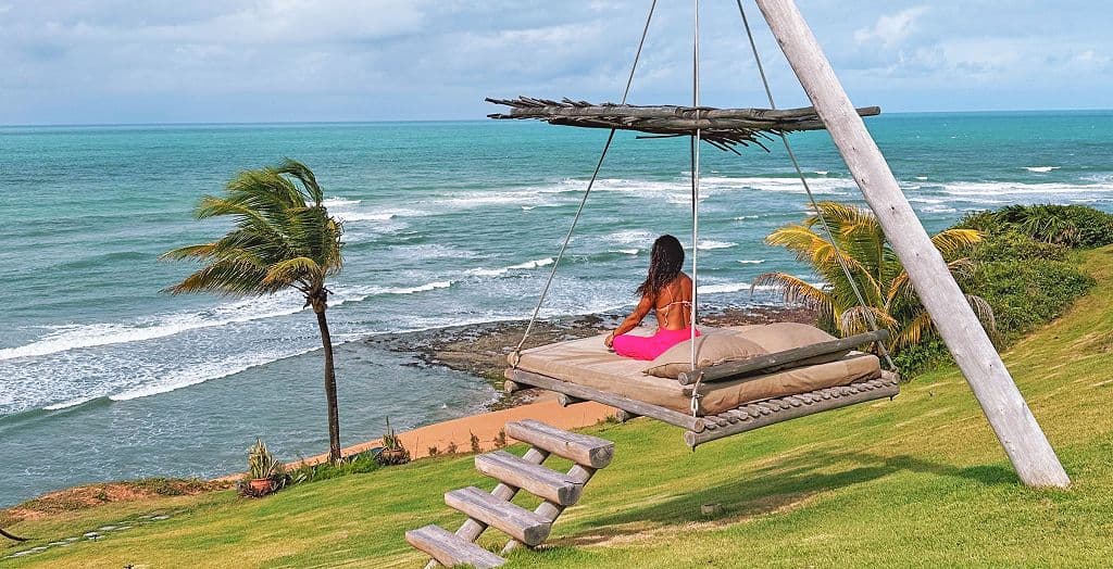 Hóspede sentada em uma cama suspensa no gramado do Kilombo Villas, de frente para o oceano