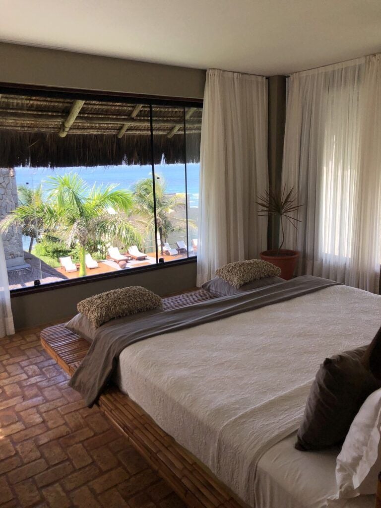 Quarto com cama king e ampla janela com vista para terraço e mar