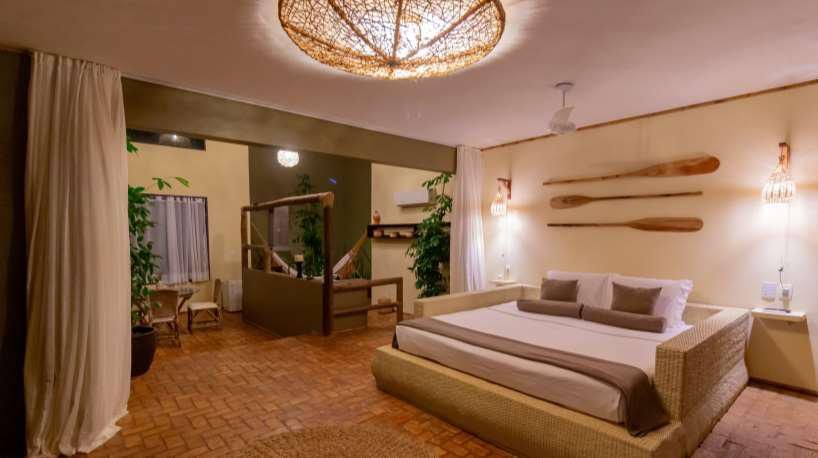 Quarto iluminado à noite com cama em estrutura de vime, remos decorativos e acesso à área externa