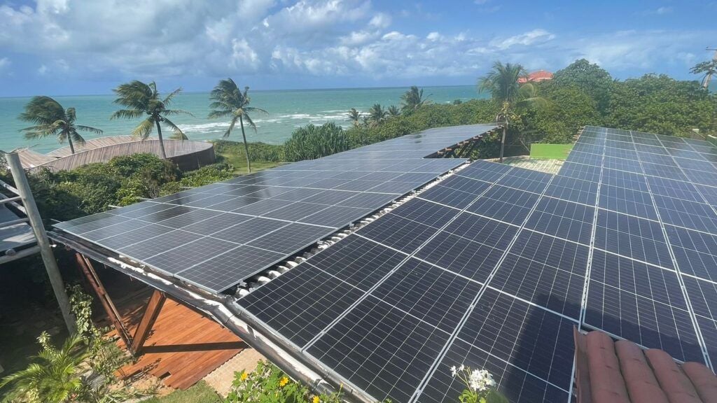 Área de cobertura solar com painéis fotovoltaicos e vista para o oceano em dia ensolarado