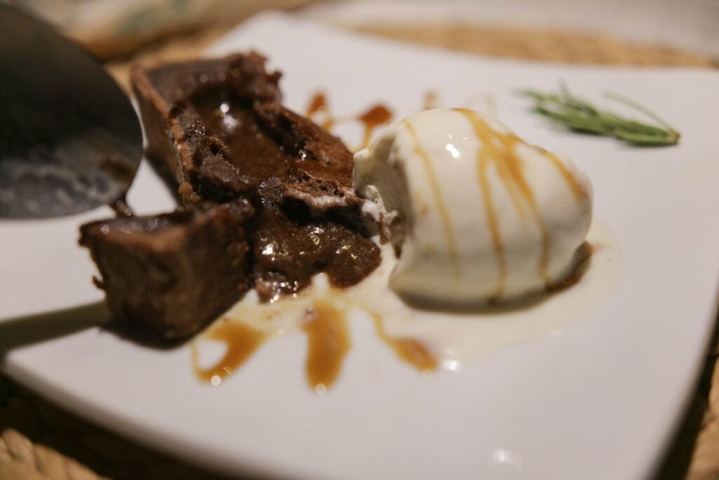Brownie de chocolate quente com sorvete de creme e calda de caramelo em prato branco