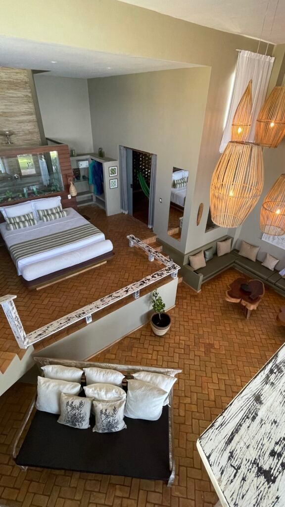 Vista interna de villa com mezanino, cama, rede e luminárias de vime
