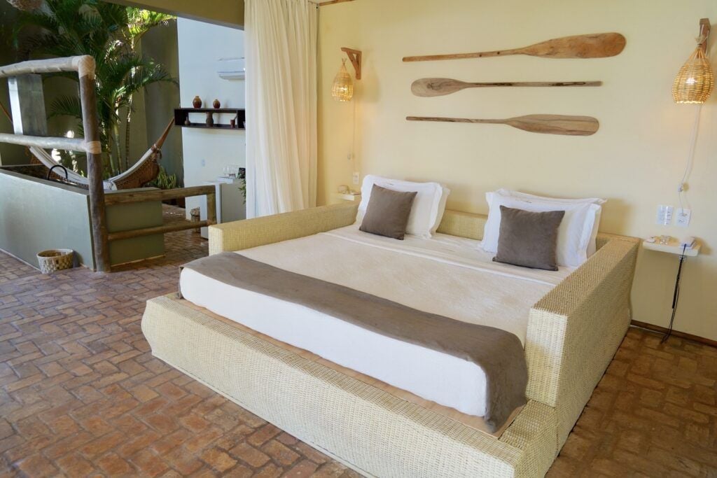 Quarto amplo com cama em estrutura de vime, remos decorativos e área externa com rede