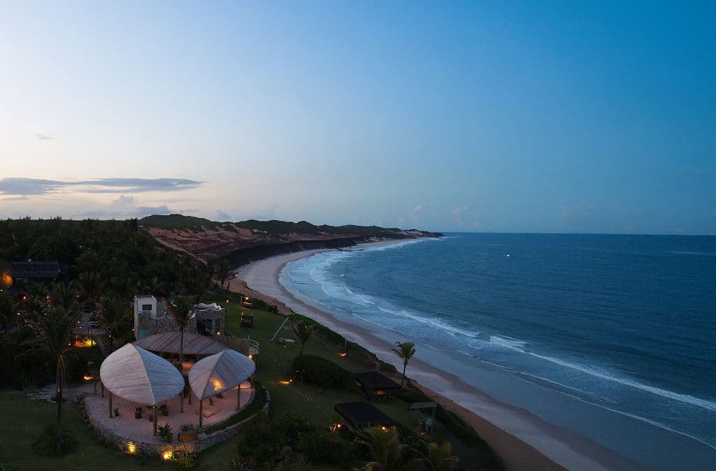 Vista aérea ao entardecer do Kilombo Villas iluminado, com a praia e o oceano ao lado