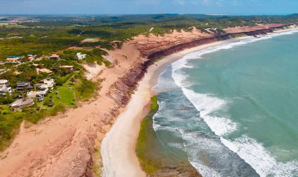 Vista aérea do litoral de Sibauma com falésias vermelhas, praia rosada e oceano turquesa