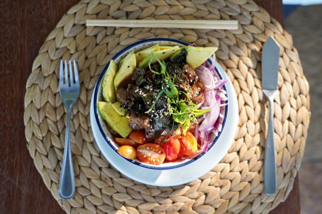 Poke bowl com atum, abacate, tomate cereja, cebola roxa e algas em tigela com palitinhos