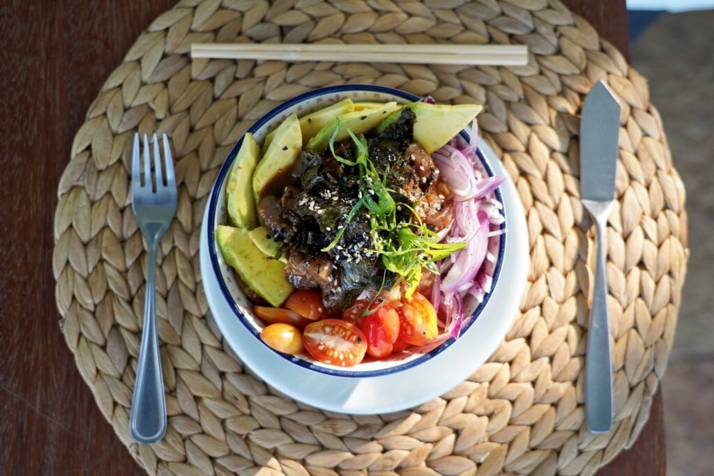 Poke bowl com atum, abacate, tomate cereja, cebola roxa e algas em tigela com palitinhos