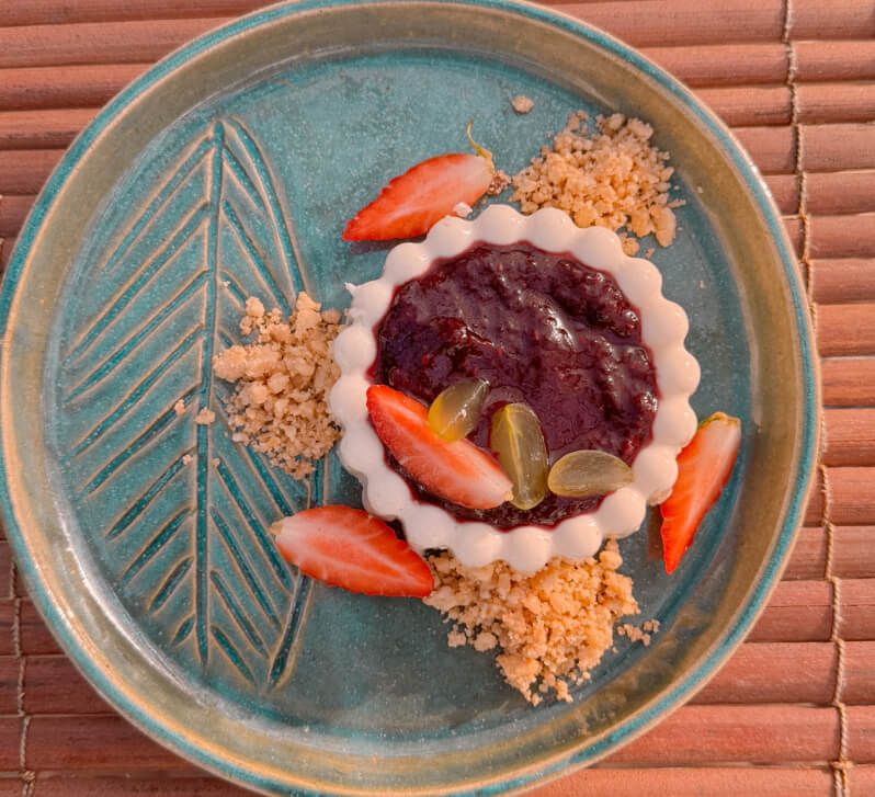 Sobremesa com coulis de frutas vermelhas em prato cerâmico turquesa decorado com folha