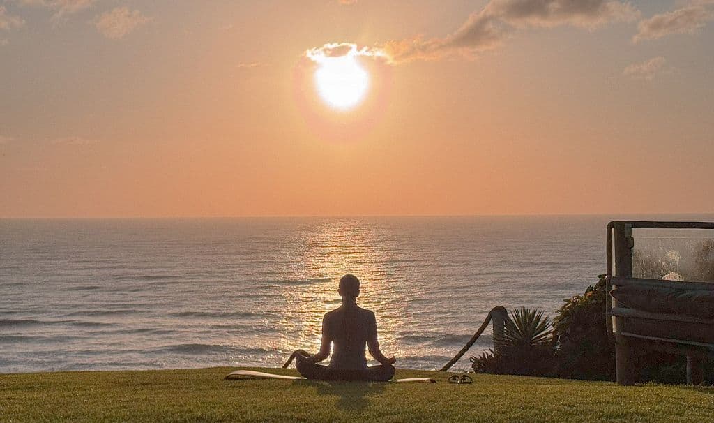 Pessoa praticando meditação em frente ao mar durante o pôr do sol