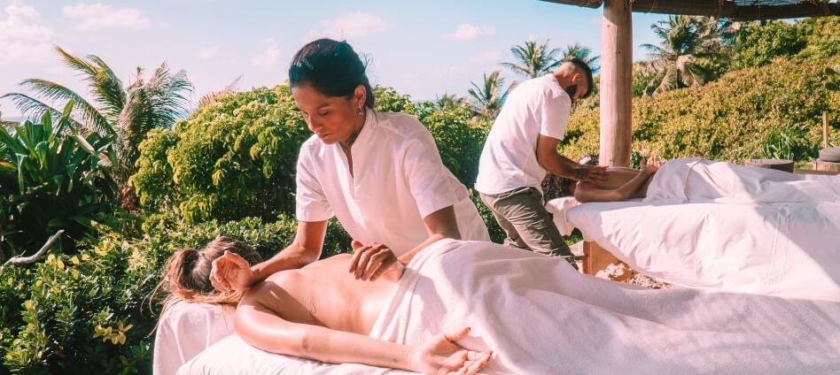 Duas massagistas realizando massagem ao ar livre com jardim tropical ao fundo